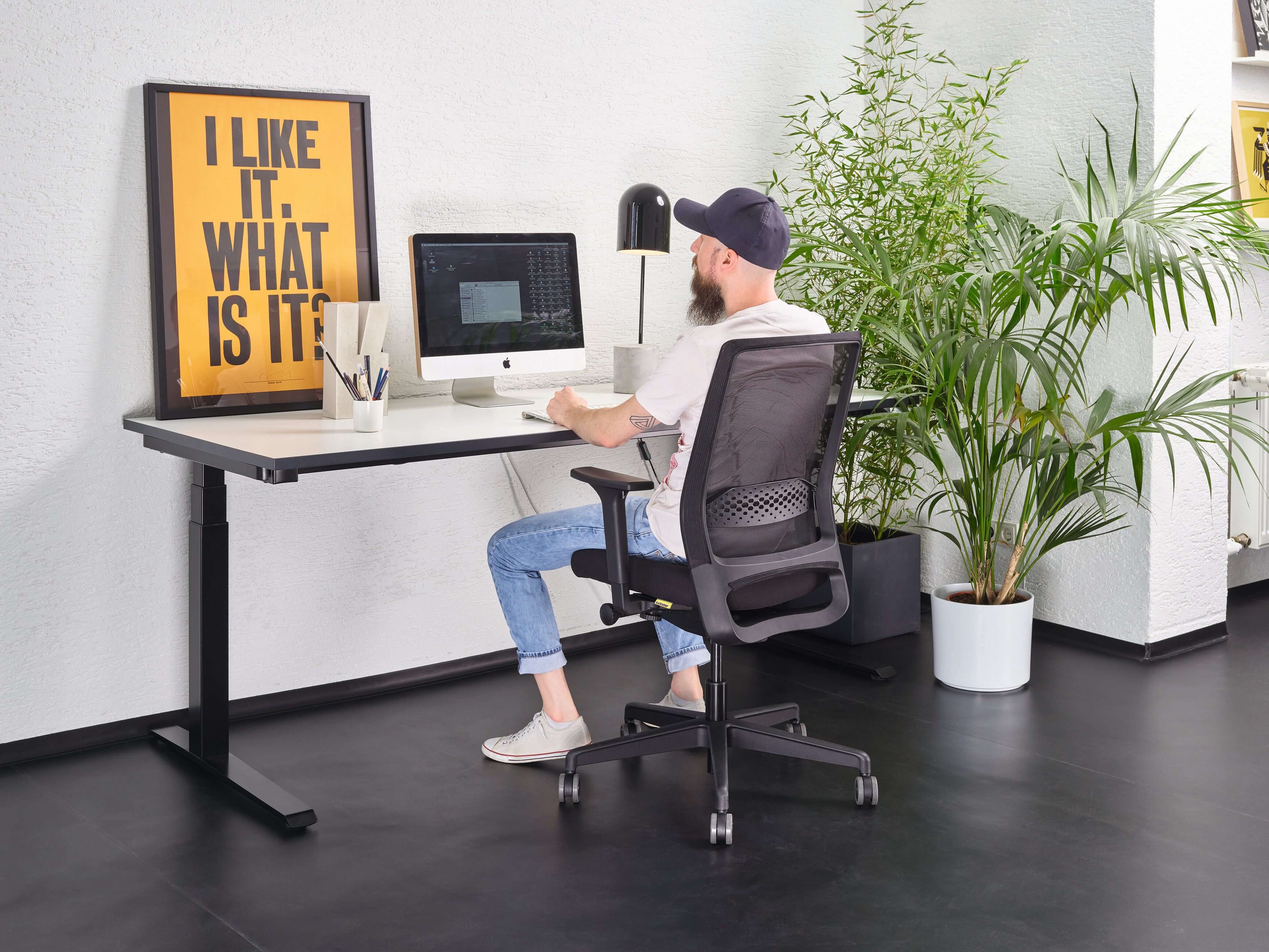A man sitting at a desk using an ergonomic office chair with lumbar support, working on a computer in a bright office space.